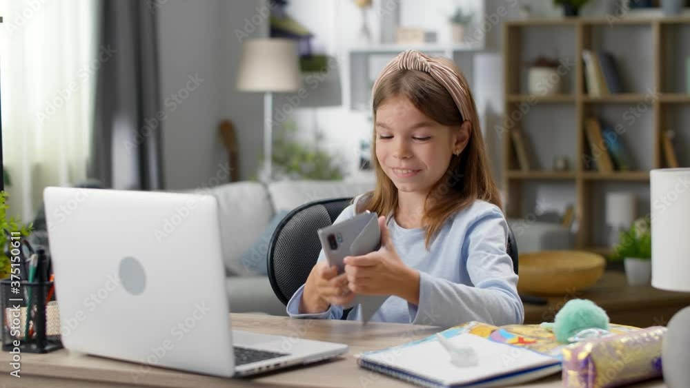 Girl playing a game on the phone during an online lesson at home in the living room Girl playing a game on the phone during an online lesson at home in the living room