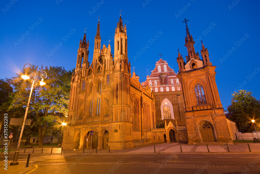 Night view of illuminated Gothic style St. Anne Church at Maironio Street in the Old Town of Vilnius, Lithuania. Church of St. Francis and St. Bernard in the background.