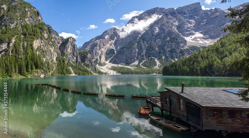 Panoramic view of the Lake Braies, Pragser Wildsee, lake in the Prags Dolomites, South Tyrol, Italy. Detail of rowboats moored in line on pristine water near a wooden cabin and mountains 