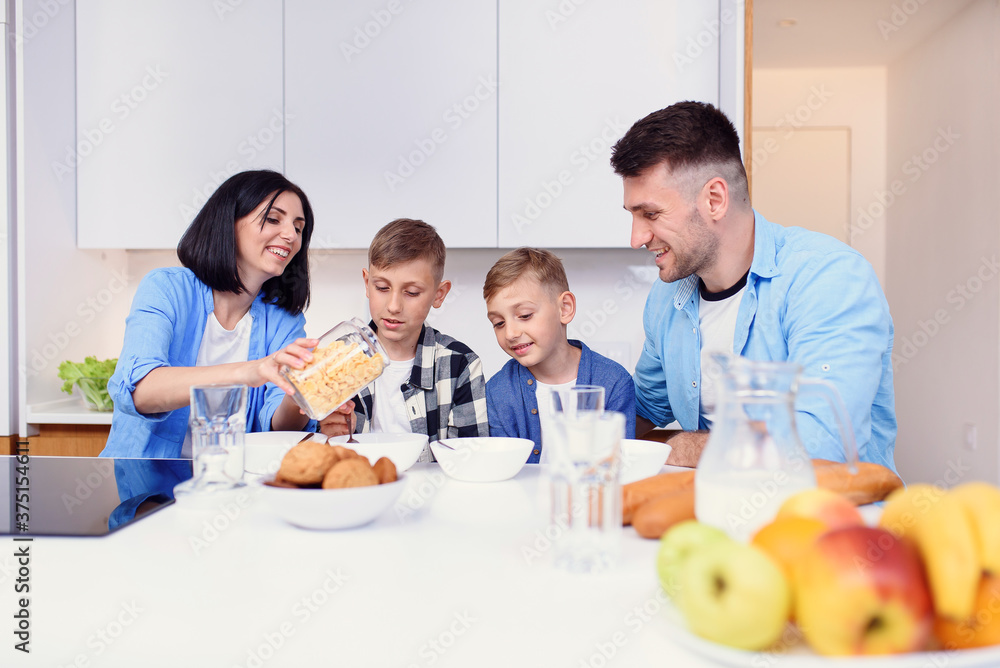 Happy family with two sons eating healthy morning breakfast with cornflakes and milk on cozy kitchen at dining table.
