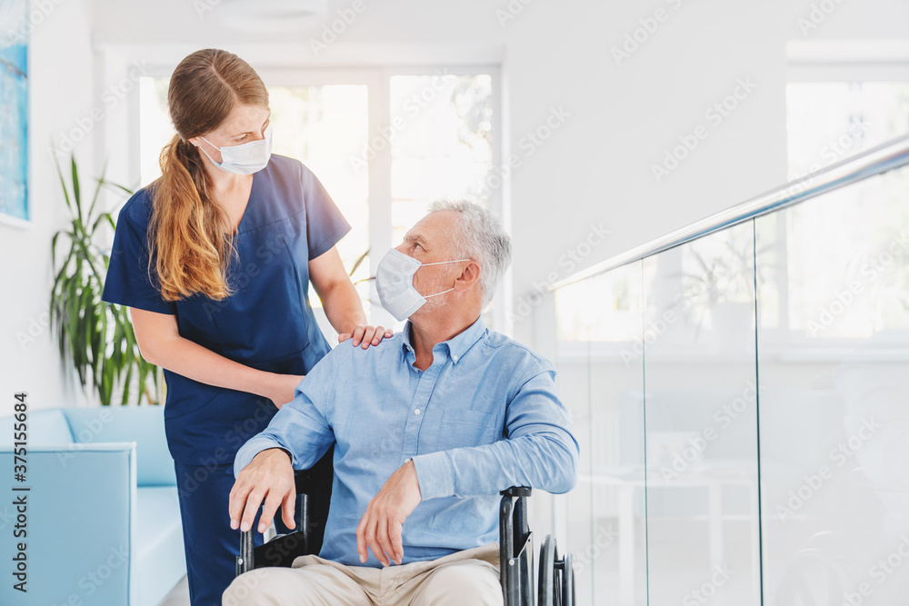 Obraz premium Young woman nurse explaining information to man patient in wheelchair in medical face mask while talking together in hospital. Epidemic and virus concept