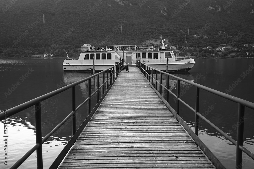 Touristic boat moored on a pier of Idro Lake (Lombardy, Brescia Province, Northern Italy). Is a small glacial lake, at the border with Trentino region. Black and white photo.