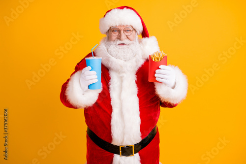 Portrait of his he nice cheerful cheery funny white-haired Santa eating fastfood menu recipe weight loss diet isolated over bright vivid shine vibrant yellow color background