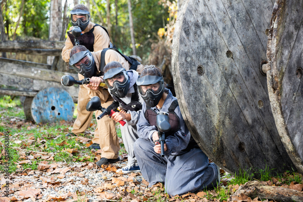 Men and women in protective uniform playing paintball on shooting range