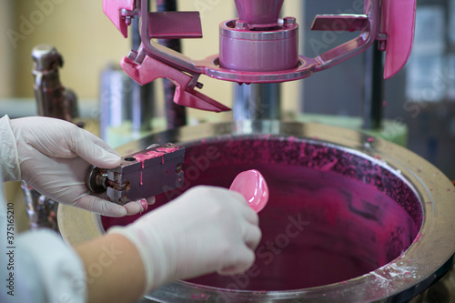 Fototapeta Naklejka Na Ścianę i Meble -  Manufacturing paint in a factory. Pink colored paint in an industrial environment.  A worker wearing rubber gloves working with liquids