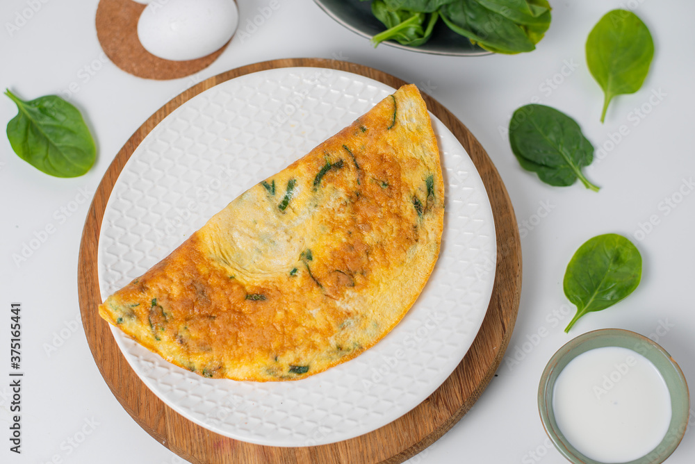 Tasty homemade omelet with green leaves spinach on a white background. Top view. Idea recipe for a healthy diet breakfast. Concept of losing weight. Easy to cook. Protein for a vegetarian. Tasty homemade omelet with green leaves spinach on a white background. Top view. Idea recipe for a healthy diet breakfast. Concept of losing weight. Easy to cook. Protein for a vegetarian.