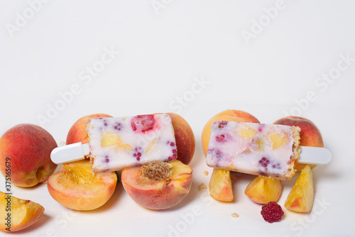 fresh summer ice cream on a stick with peach and raspberry berries . on a light background top view . ice cream ingredients ripe peaches and raspberries with yogurt