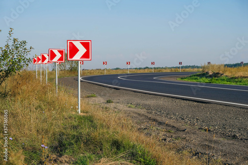 A series of road signs on a sharp turn. Red and white.