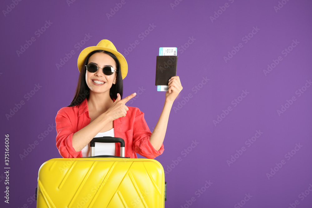 Beautiful woman with suitcase and ticket in passport for summer trip on purple background. Vacation travel Beautiful woman with suitcase and ticket in passport for summer trip on purple background. Vacation travel