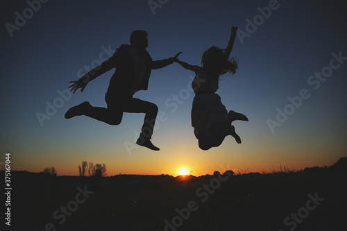 silhouette of young couple are jumping and having fun outdoors in the field on summer evening. romantic photo at sunset time. love story