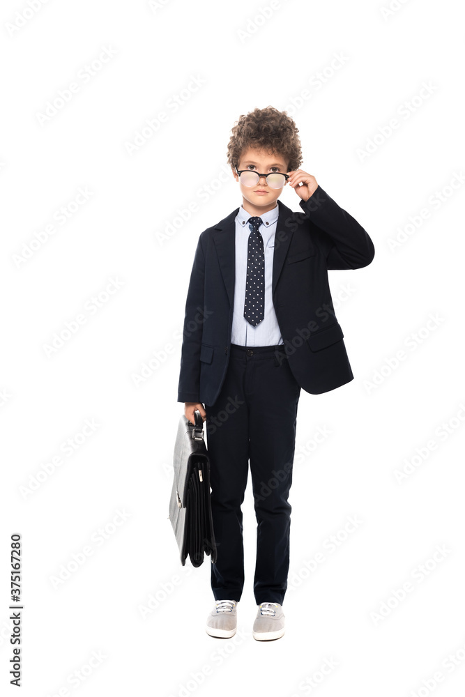 curly boy in suit touching glasses and holding briefcase isolated on white curly boy in suit touching glasses and holding briefcase isolated on white