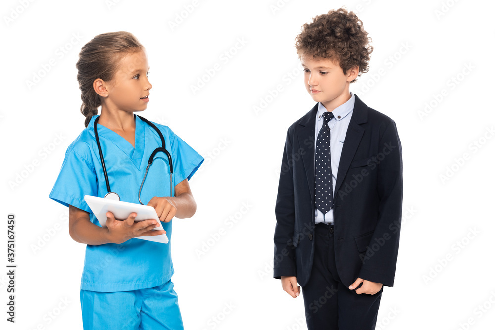 child in costume of doctor using digital tablet near curly boy in formal wear isolated on white child in costume of doctor using digital tablet near curly boy in formal wear isolated on white
