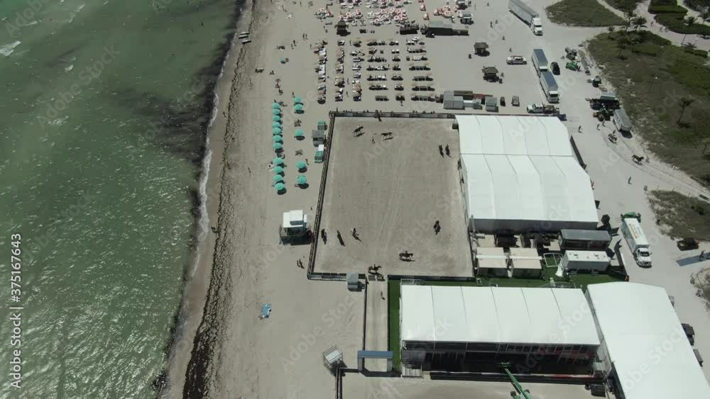 This is a straight forward, upwards pan drone shot of of Miami Beach, Florida, USA. Horses are running in the early part of the shot, and then we can see some beach tents and people enjoying their day This is a straight forward, upwards pan drone shot of of Miami Beach, Florida, USA. Horses are running in the early part of the shot, and then we can see some beach tents and people enjoying their day