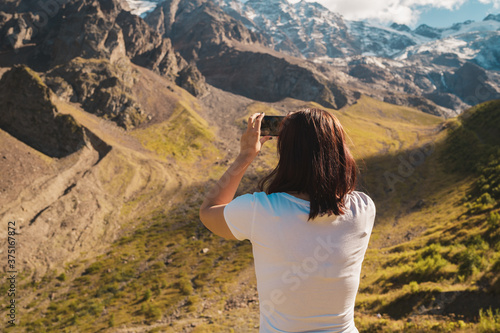 Young woman takes pictures of mountain landscape on smartphone. Female tourist photographing mountains on mobile phone.