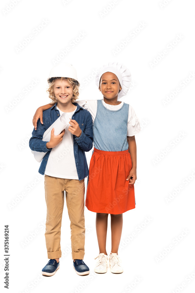 african american kid in chef hat hugging curly boy in safety helmet and costume of architect standing with blueprint isolated on white african american kid in chef hat hugging curly boy in safety helmet and costume of architect standing with blueprint isolated on white