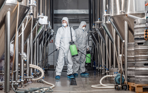 Quarantine and prevention on factory. Man in protective suit disinfects beer kettles