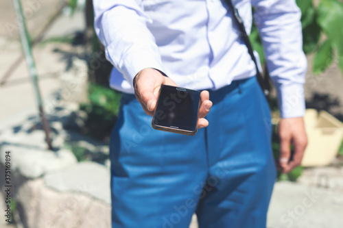 A young man holds a phone in his hands on the street. Businessman holds the phone in his hands on the street.