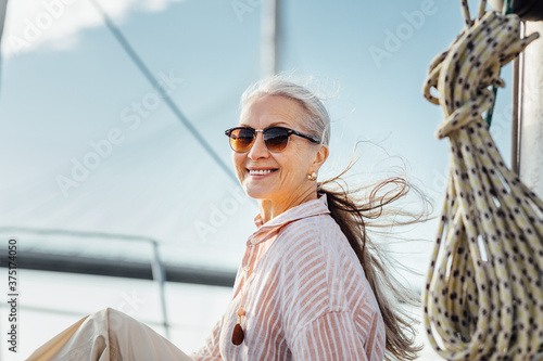 Portrait of a happy mature woman wearing sunglasses on a yacht. Beautiful female with long hair looking at camera while enjoying a boat trip.