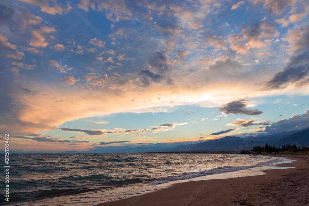Fototapeta premium Beautiful sunset by the lake. Bright clouds are reflected in the water. Kyrgyzstan.