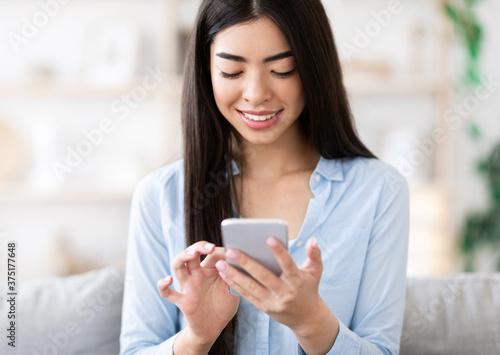 Smiling korean girl using smartphone at home  checking incoming emails
