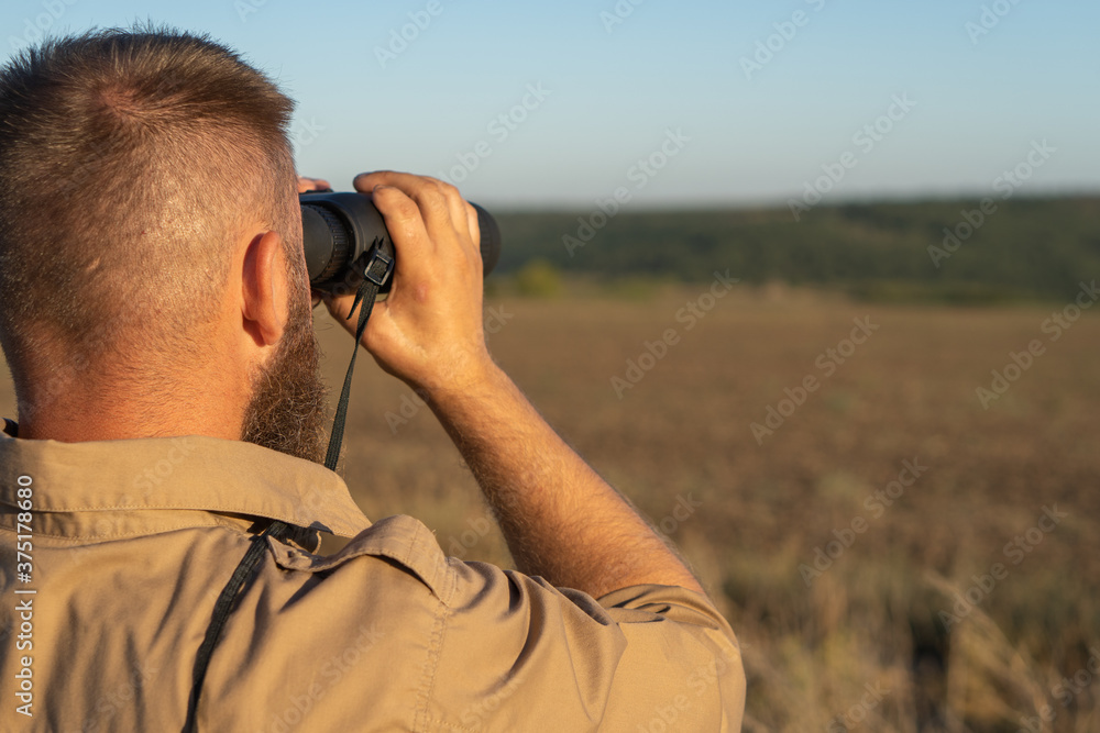 A bearded man looks through binoculars, close-up. The hunter uses binoculars to search A bearded man looks through binoculars, close-up. The hunter uses binoculars to search