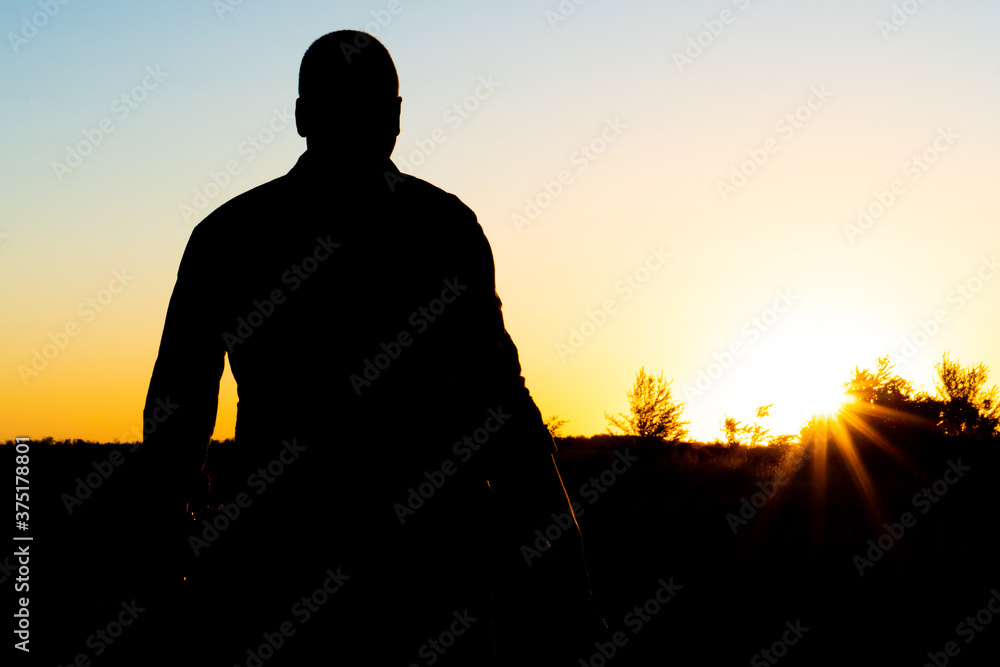 Silhouette of a man with a weapon in his hands on a sunset background