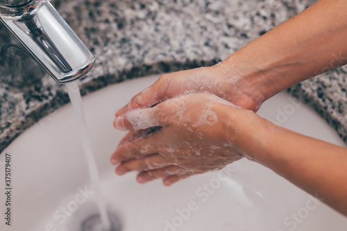 Cleaning Hands. Washing hands thoroughly. Washing hands twenty seconds with soap. Young woman washing hands with soap over sink in bathroom. Covid-19. Coronavirus. photo