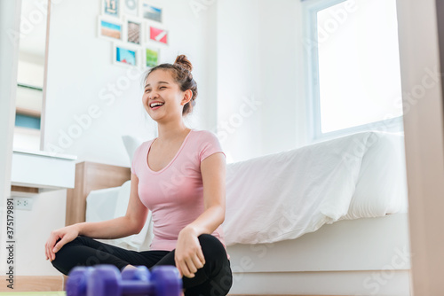 Happy women in sportswear clothes meditate on yoga mat in bedroom after exercising. Beautiful young woman exercises in home. 