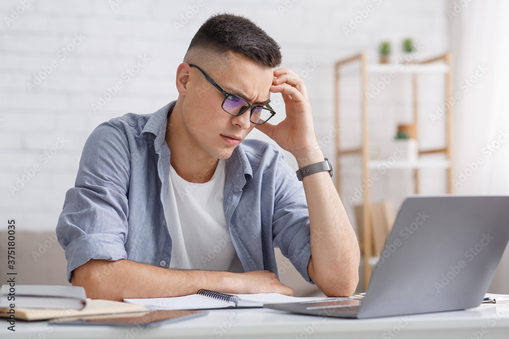 Complicated question and online education. Serious guy thinks and looks at laptop Complicated question and online education. Serious guy thinks and looks at laptop