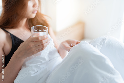 A woman with a fever is taking cold medicine in bed. 
