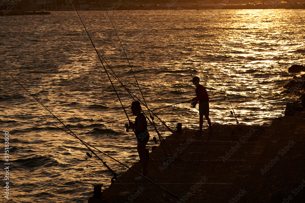two people fish on the pier at dusk