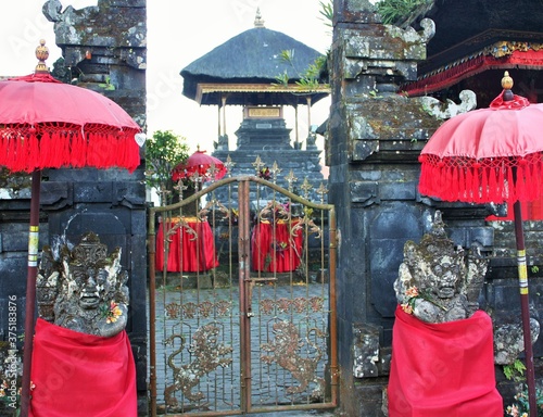 Entrance to Balinese temple with gate guardian stone statues covered in red cloth with red parasols photo