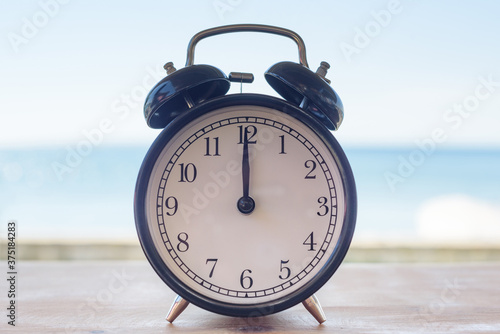 black retro alarm clock stands on the table against the background of the sea