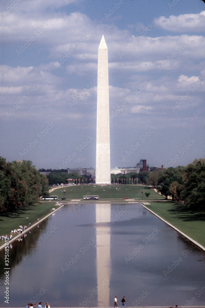 Washington Memorial in Washington DC glows against a blue sky with spotted white clouds while reflecting on water  Royalty free stock photo