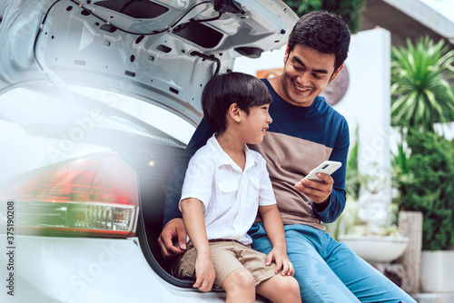 Asian father and son sitting at trunk car together.