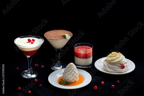 Pavlova meringue cake with fresh berries on black background. Decorated with a berry and a mint leaf. Various desserts are in the background.