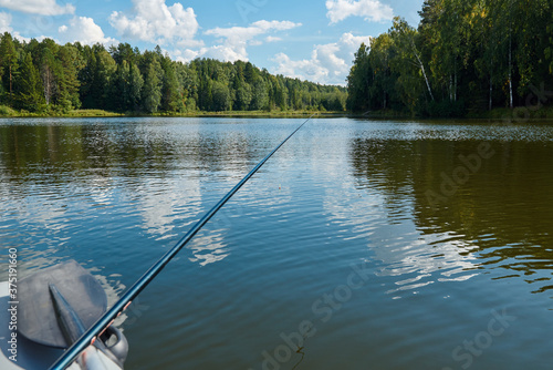 View of a pond in the countryside in summer through the eyes of a fisherman with a fishing rod
