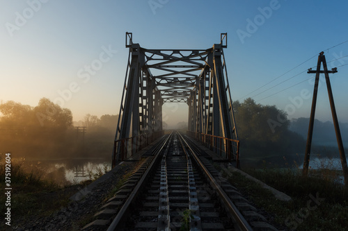 Landscape with railway and bridge. Sunrise over the misty river