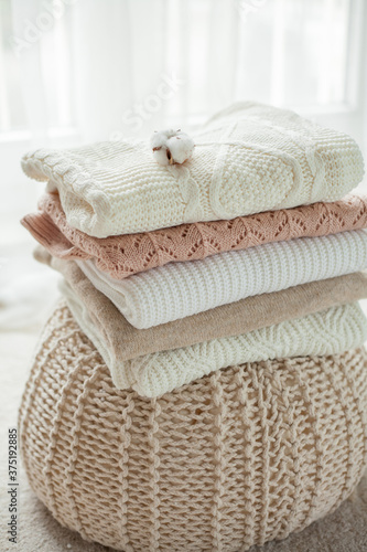 A stack of knitted sweaters, cotton. Women's sweaters lie on the ottoman. Cozy autumn clothes.