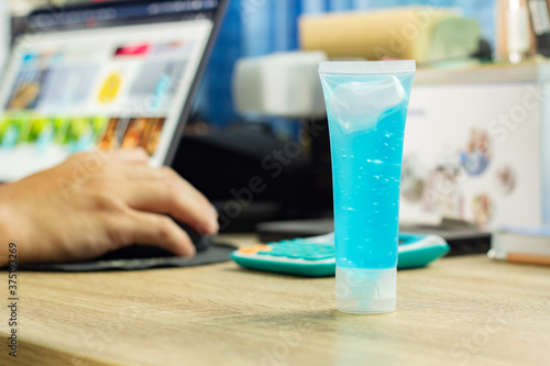 A select focus at tube of alcohol gel blue corona virus antiseptic is placed on the desk for hand clean. concept new normal now has a lap top (Note book) blur background.