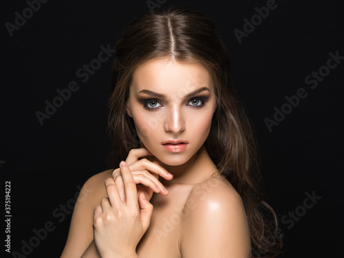 Young amazing girl with long wavy hair and sophisticated heavy makeup looking at camera isolated on black.