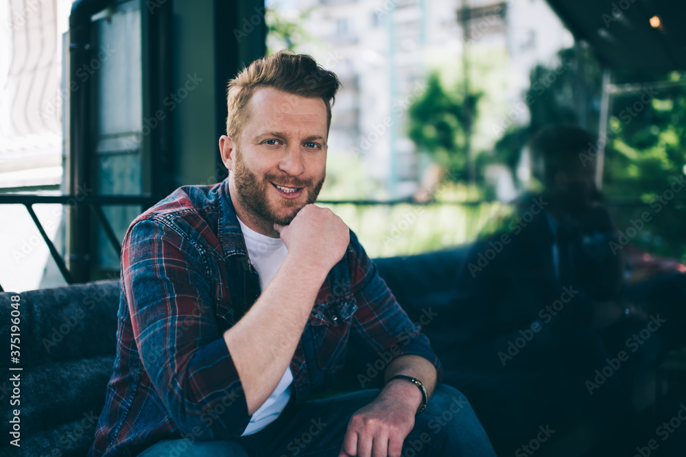 Fototapeta premium Joyful charismatic man looking at camera and smiling while relaxing on cozy balcony