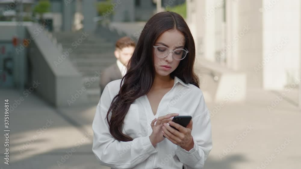 Pretty Business Woman in Eyeglasses Using Smartphone on Street of Business Center Downtown.. Attractive Young Female Employer Enjoying Using App on Mobile Phone for Social Media. Pretty Business Woman in Eyeglasses Using Smartphone on Street of Business Center Downtown.. Attractive Young Female Employer Enjoying Using App on Mobile Phone for Social Media.