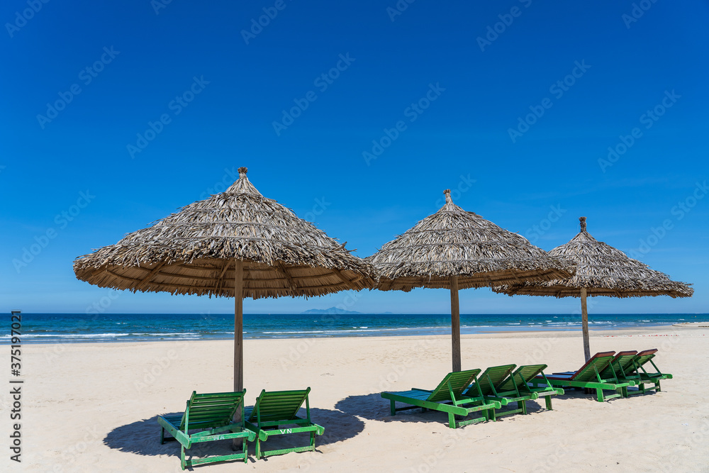 Tropical sand beach and summer sea water with blue sky and straw umbrella. Travel and nature concept