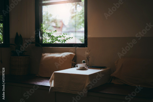 Seat in living room and white cup of coffee on wooden box cover with cloth and the sunlight shines through the window  Vintage style and dark tone