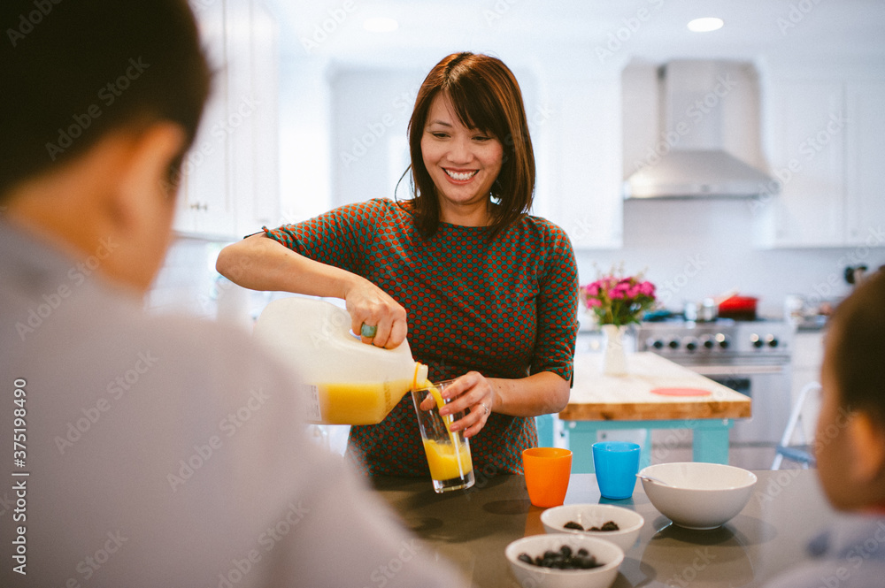 Mother smiles at family while pouring orange juice in kitchen Mother smiles at family while pouring orange juice in kitchen