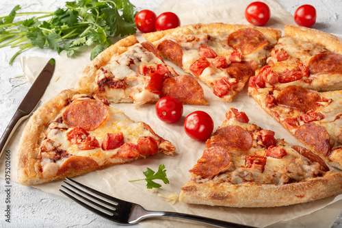 Pepperoni pizza on a light background. Pizza with sausage, tomato paste and tomatoes on a light background.