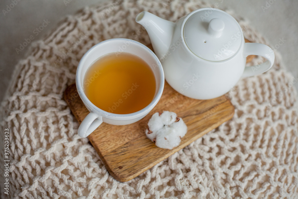 A mug of hot tea, a teapot, a wooden stand on an ottoman. Cozy autumn. Winter breakfast. Cotton. A mug of hot tea, a teapot, a wooden stand on an ottoman. Cozy autumn. Winter breakfast. Cotton.
