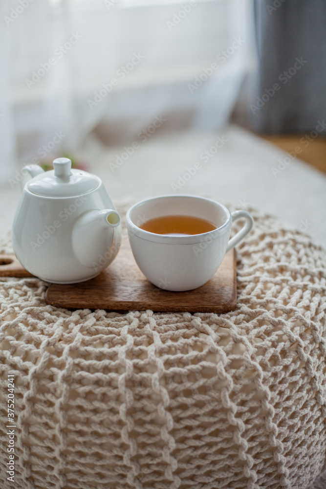 A mug of hot tea, a teapot, a wooden stand on an ottoman. Cozy autumn. Winter breakfast. Cotton.