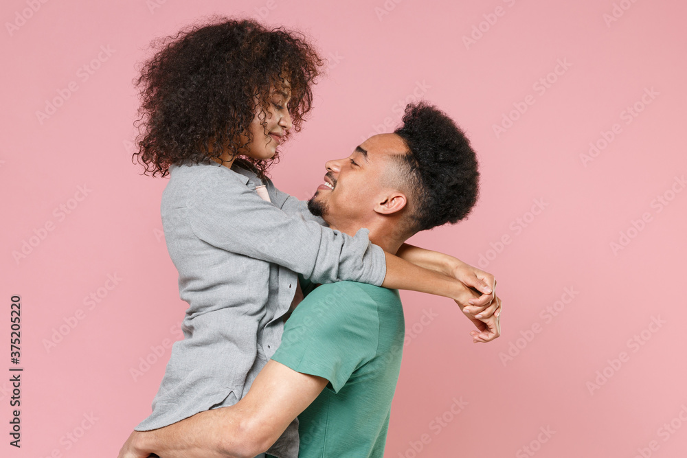Side view of smiling young african american couple two friends guy holding on hands girl in casual clothes posing looking at each other isolated on pastel pink color wall background studio portrait. Side view of smiling young african american couple two friends guy holding on hands girl in casual clothes posing looking at each other isolated on pastel pink color wall background studio portrait.